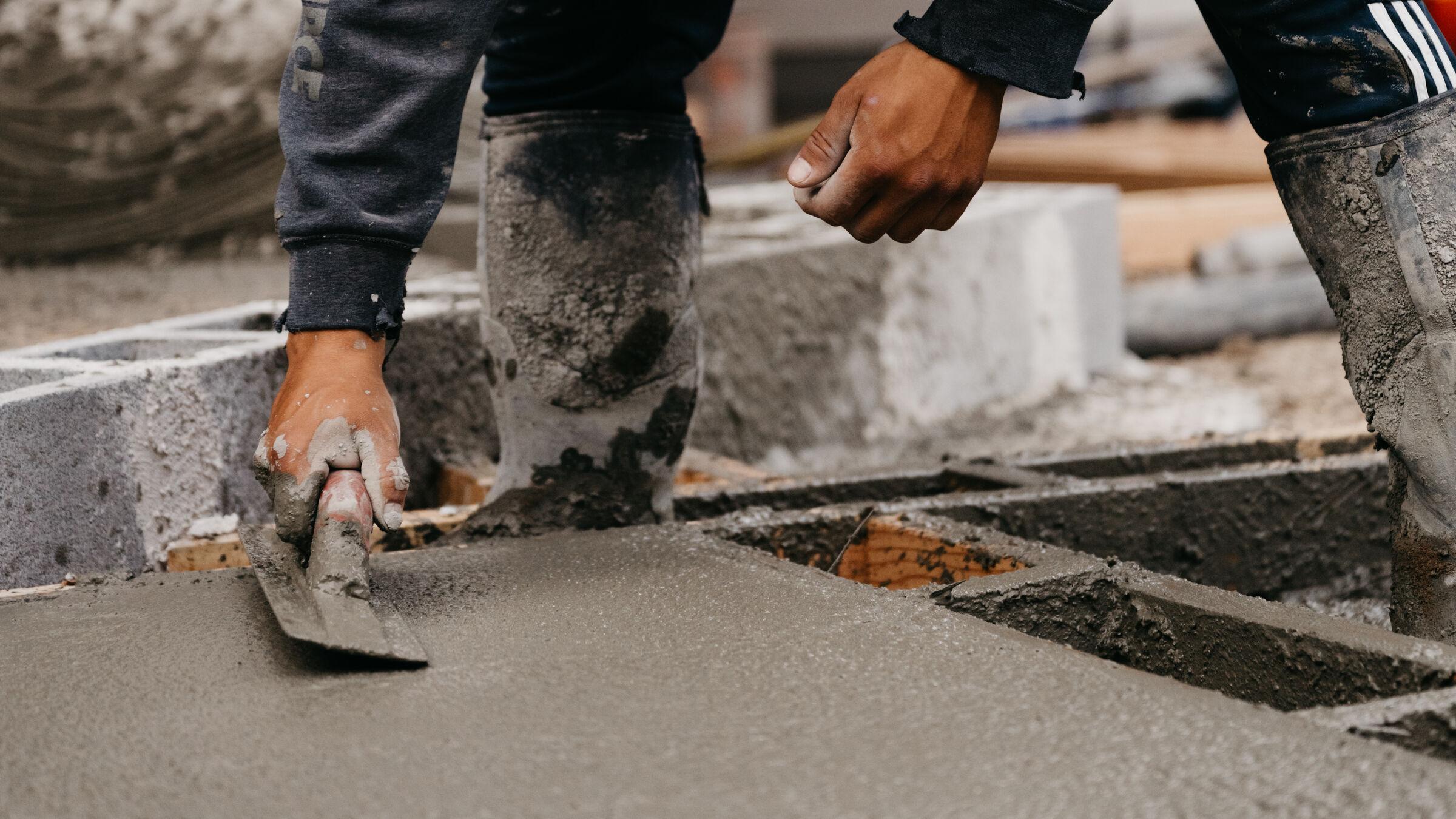 A mason floating wet concrete by hand against a formed edge