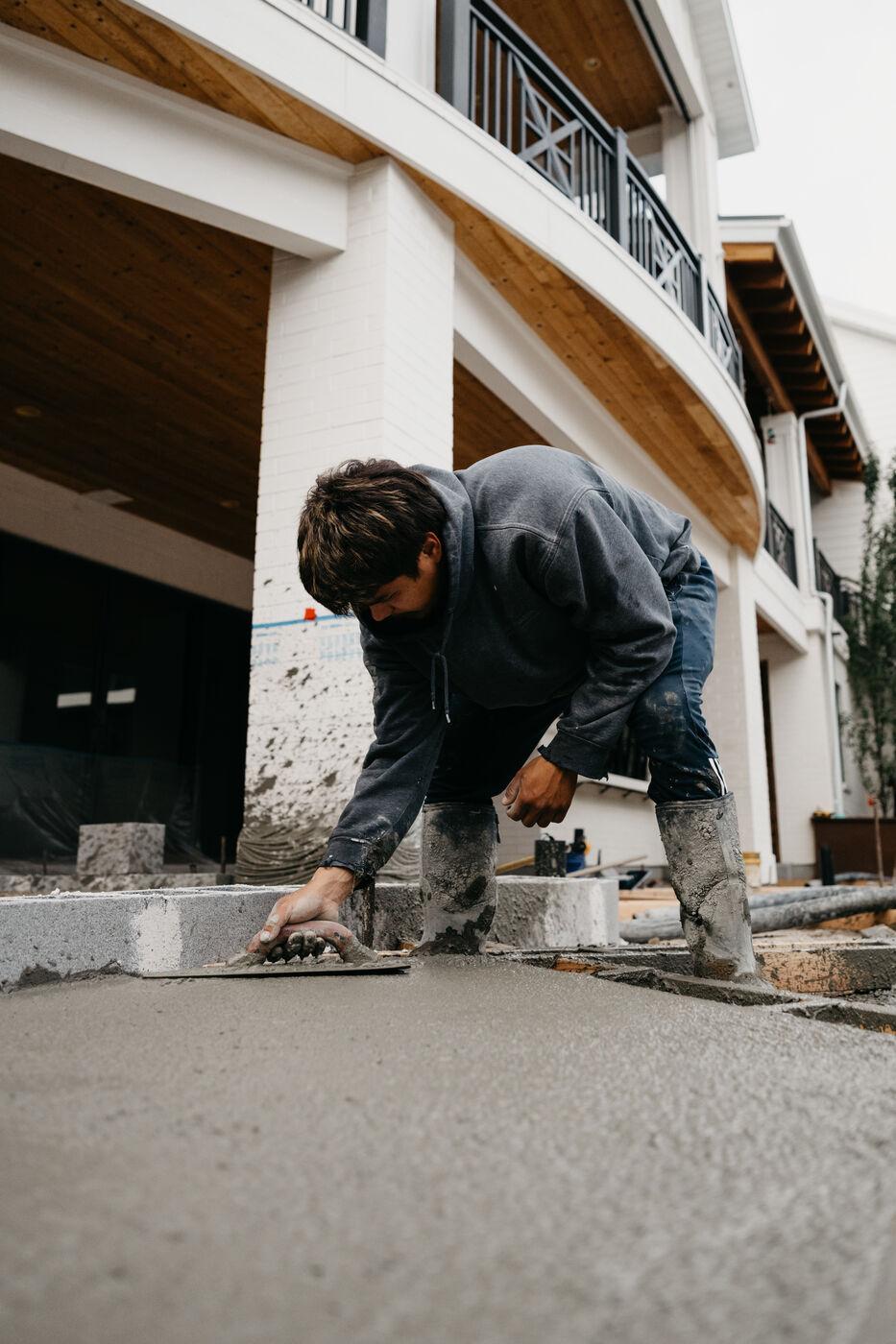 A crew member troweling a slab edge tight against the house