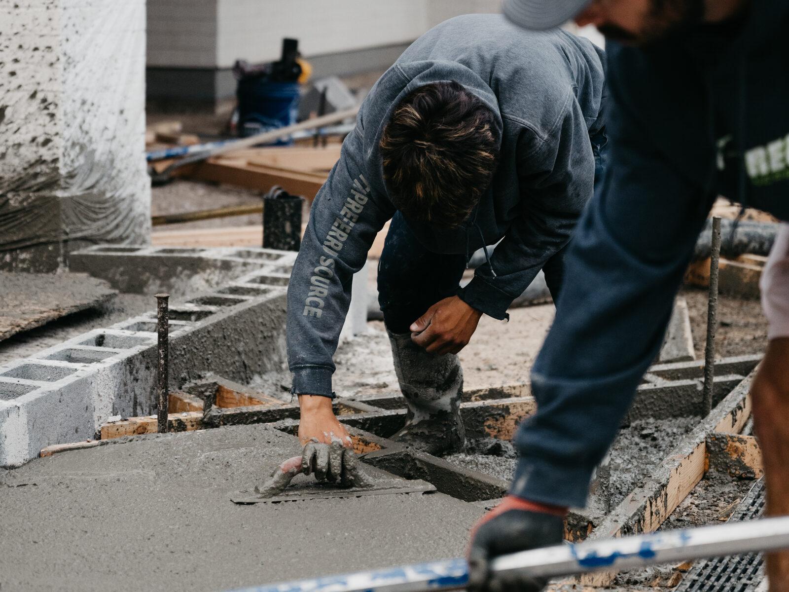 A crew member floating wet concrete by hand with a bull float on an active site