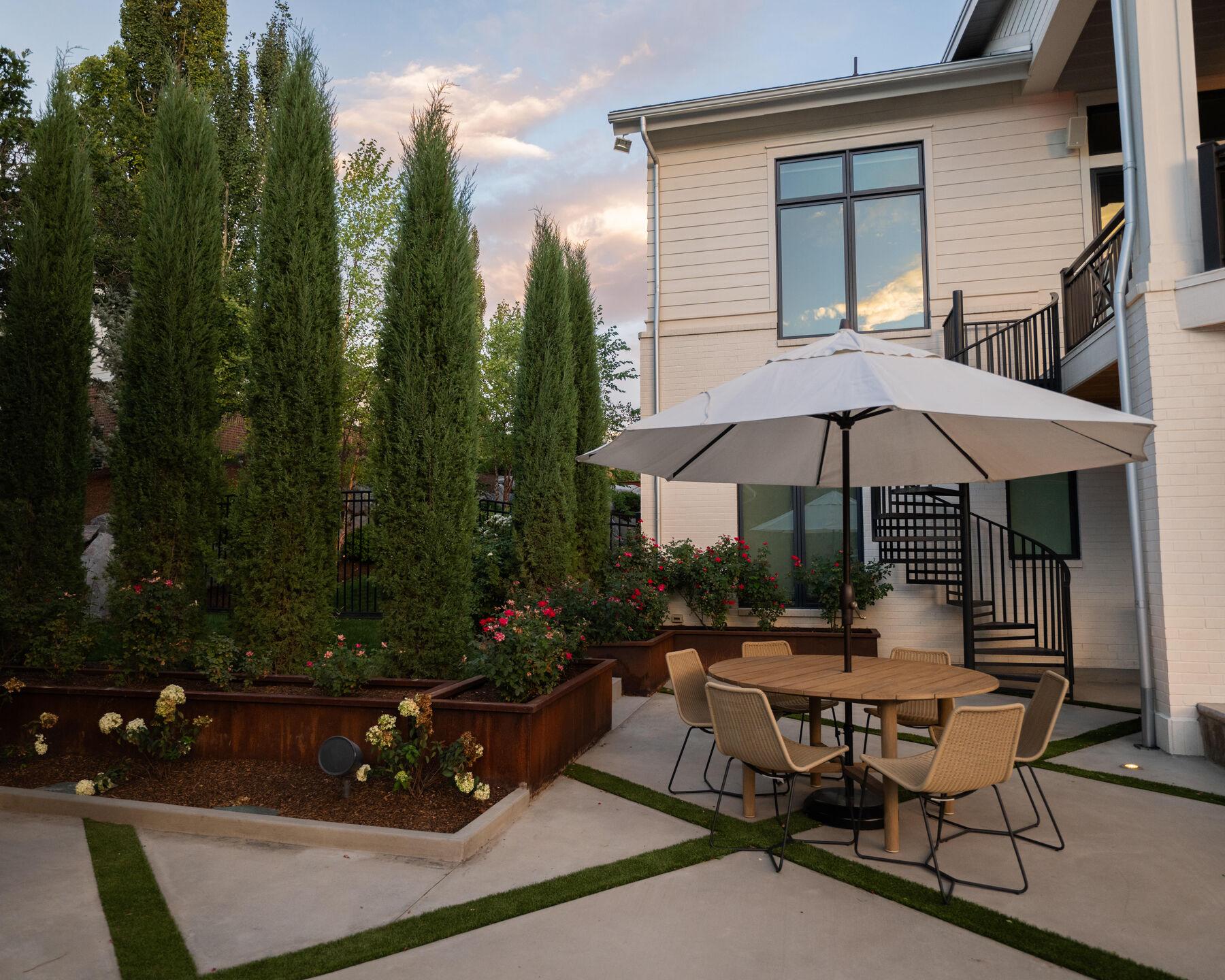 A dining terrace with corten planters and a furled umbrella at dusk