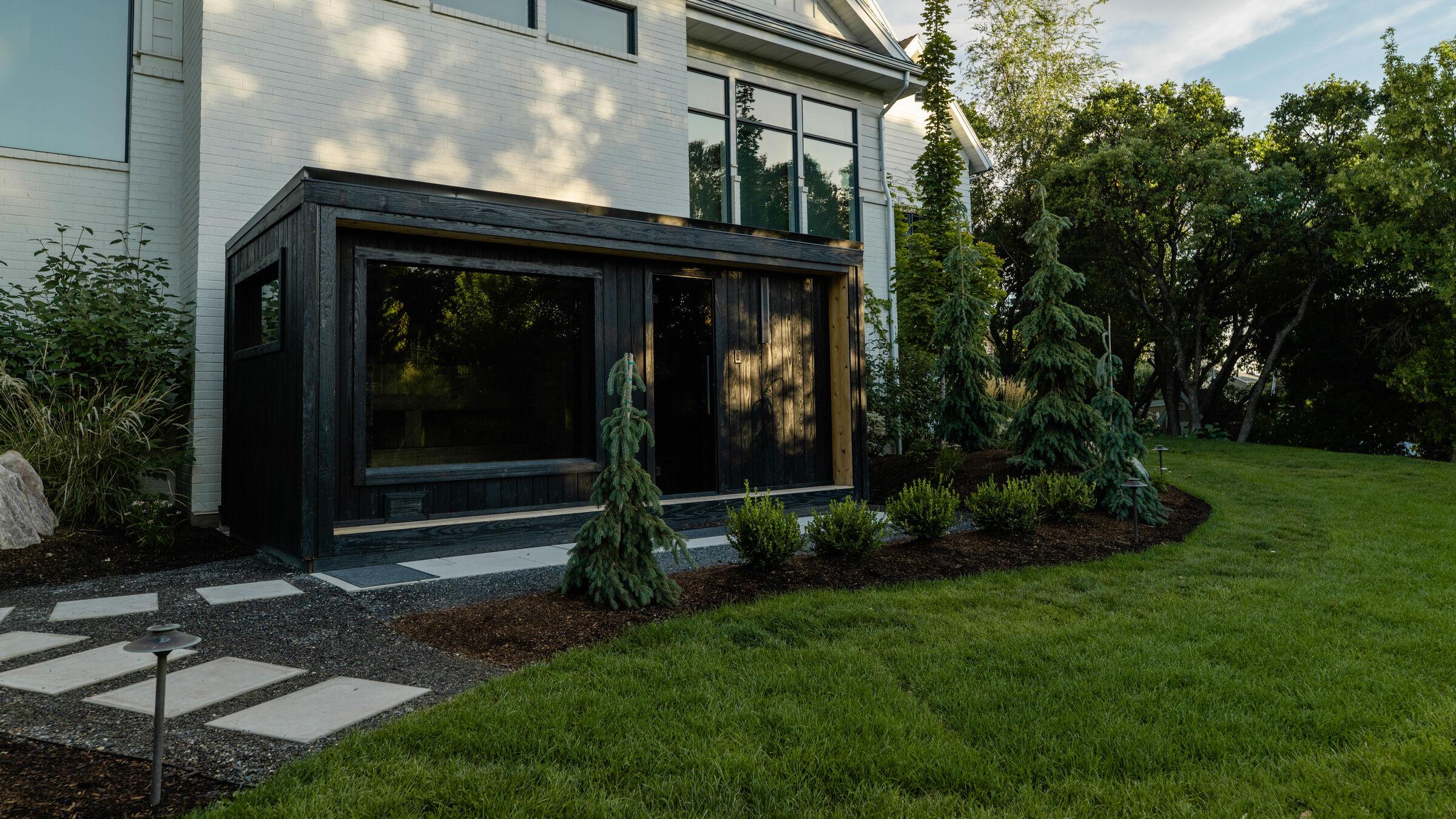A blackened-timber garden studio on lawn with a stone path to its door