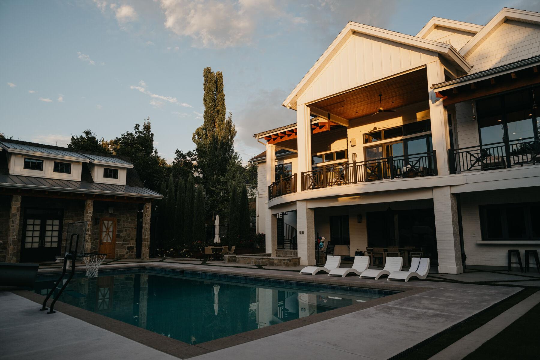The pool and house at dusk, loungers ranged along the deck