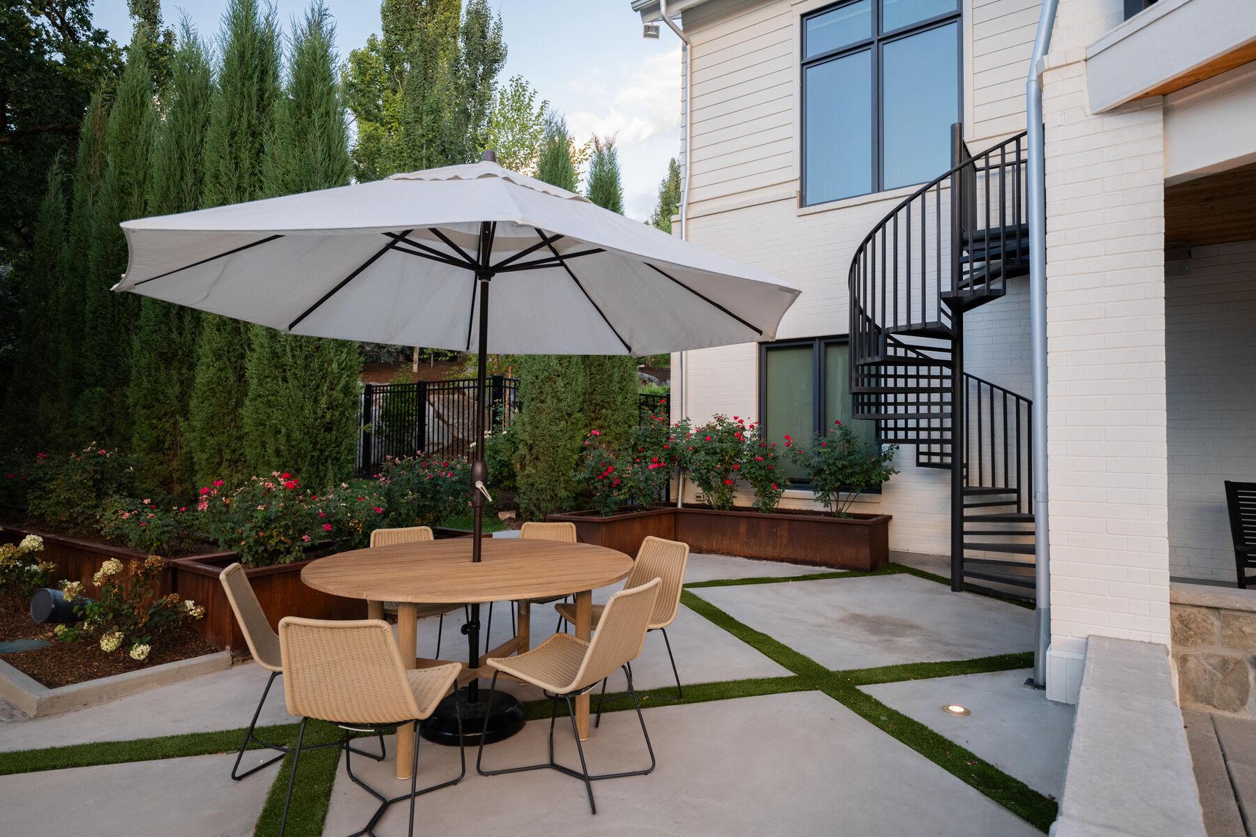 A dining terrace with umbrella and spiral stair, its paving set in turf joints