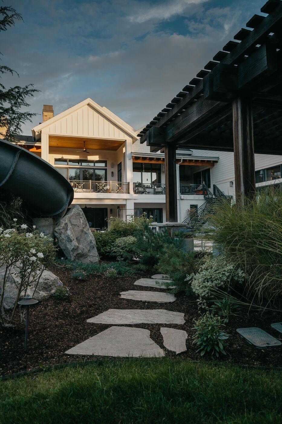 A flagstone path threading planting toward a lit house at dusk