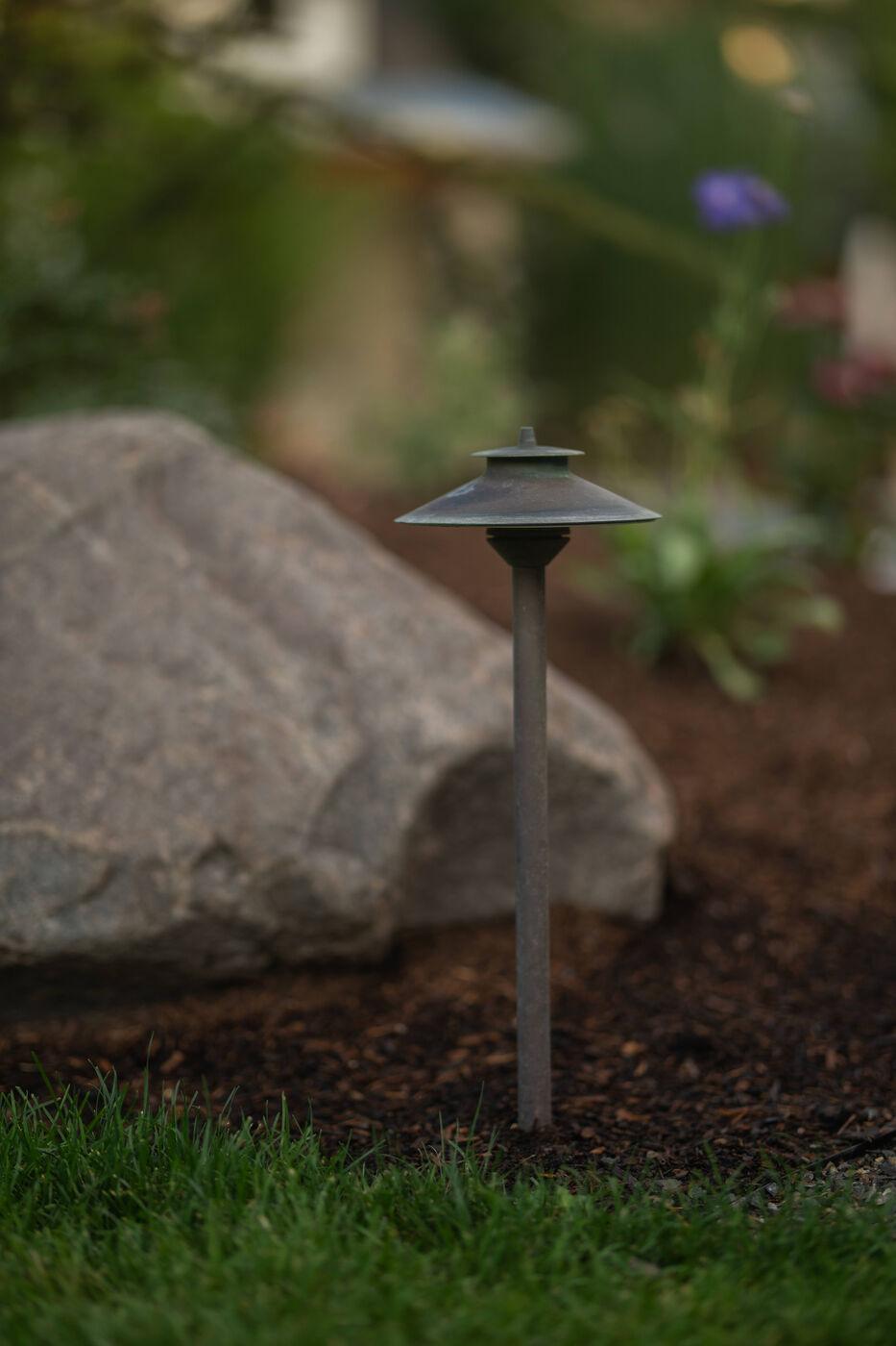 A low path light throwing a pool of light across mulch and a set boulder