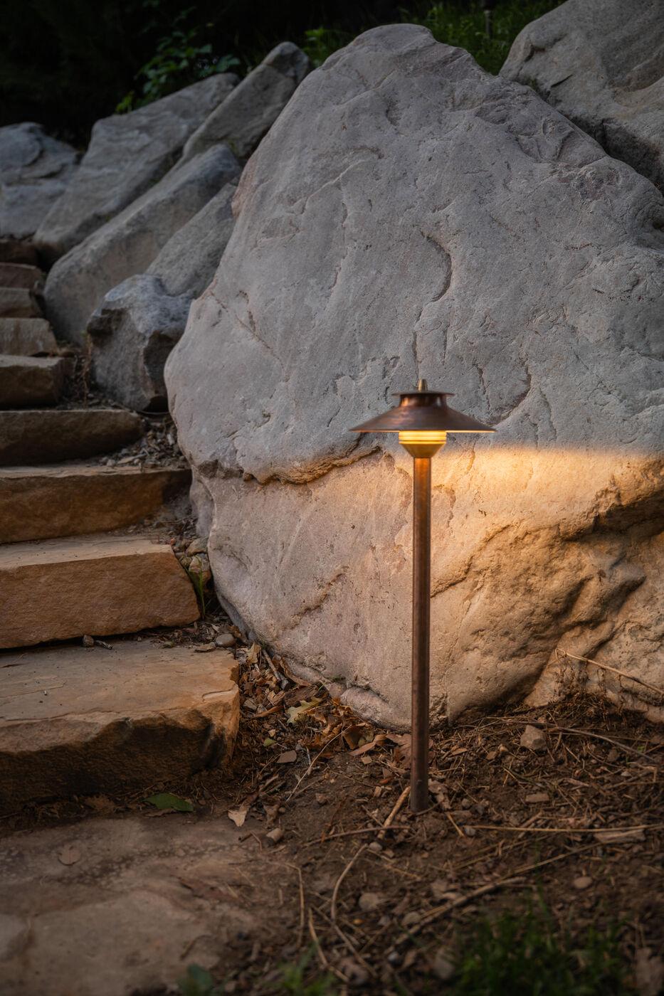 A fixture uplighting a boulder face beside stone steps after dark