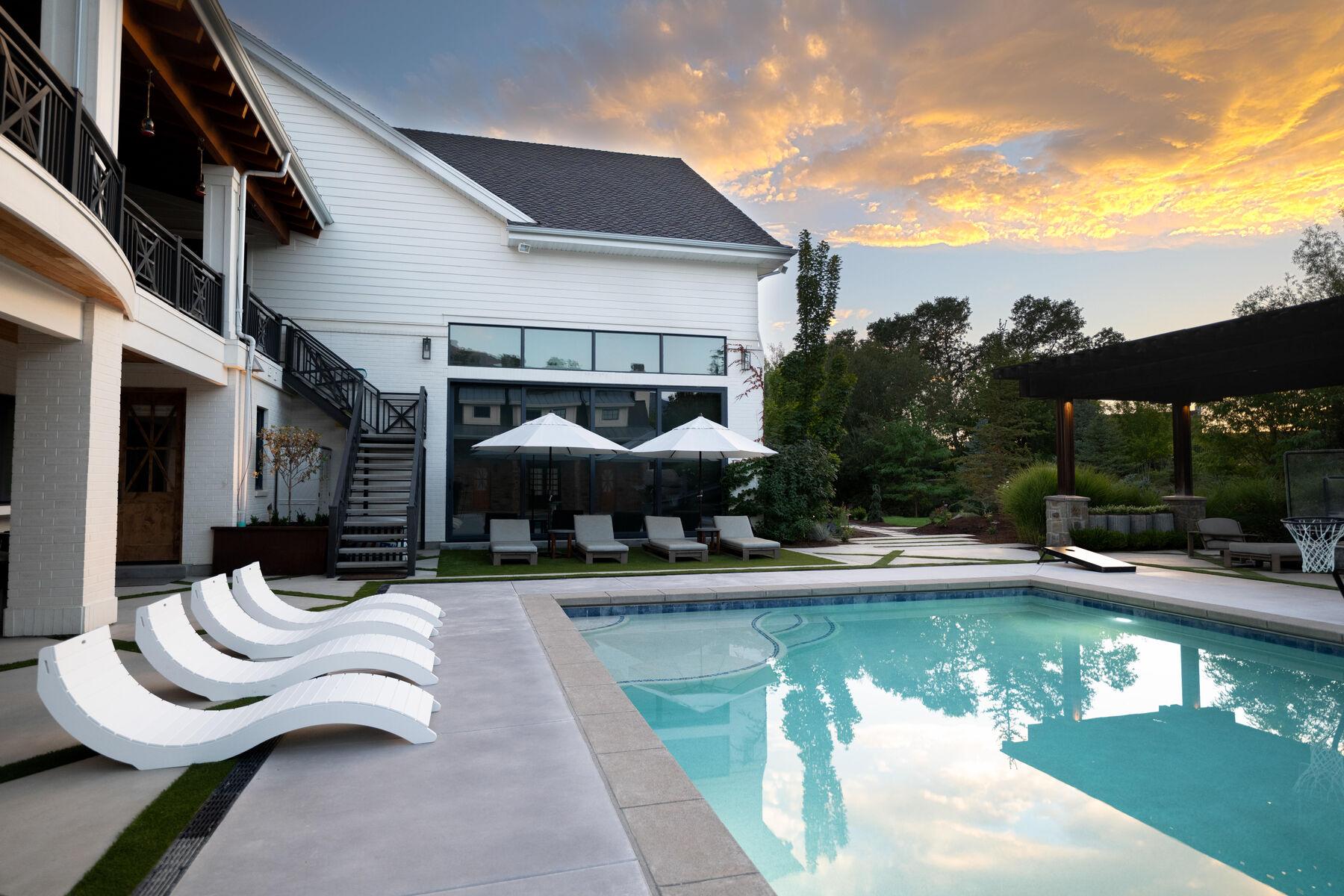 A pool at sunset with curved white loungers and a shade pergola beyond