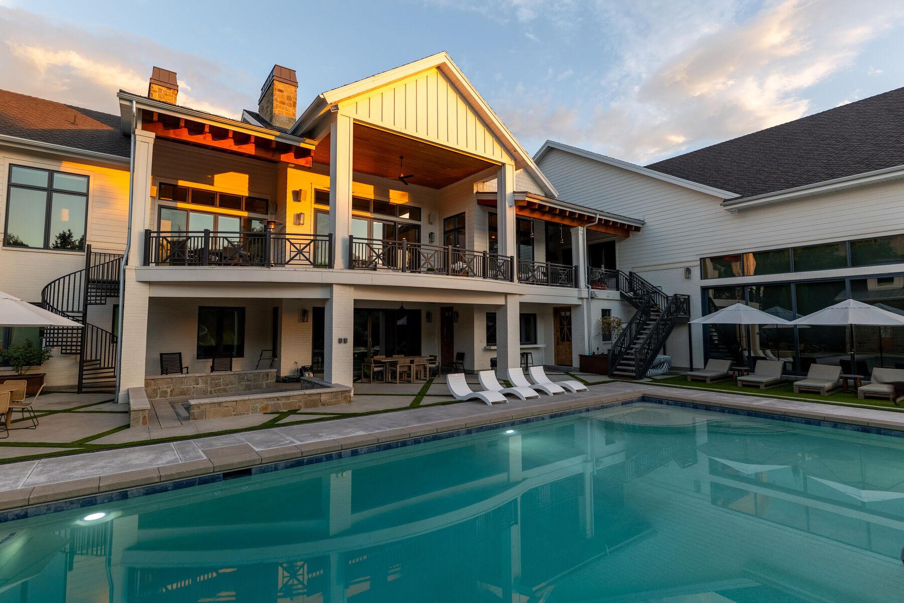A pool at golden hour below a deep timber porch and a row of umbrellas