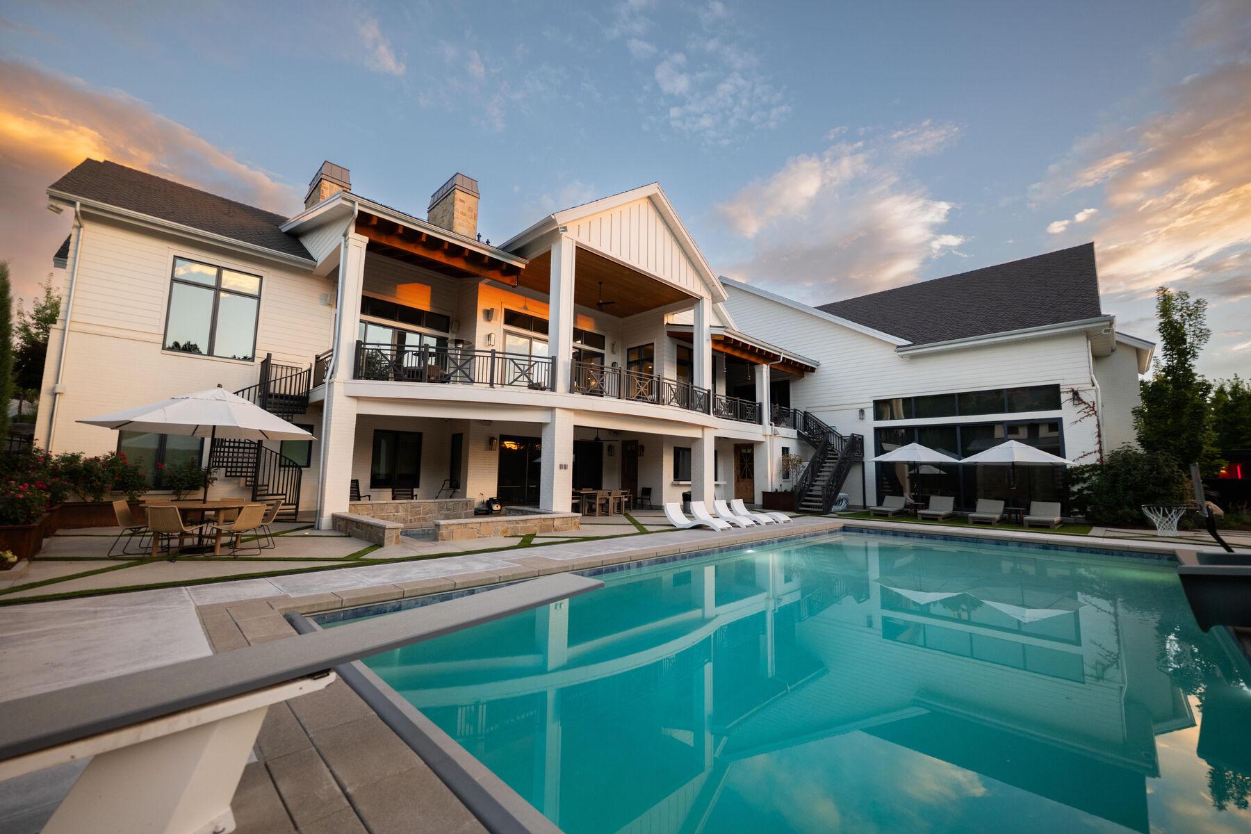 A pool at dusk with umbrellas furled and the house lit behind it
