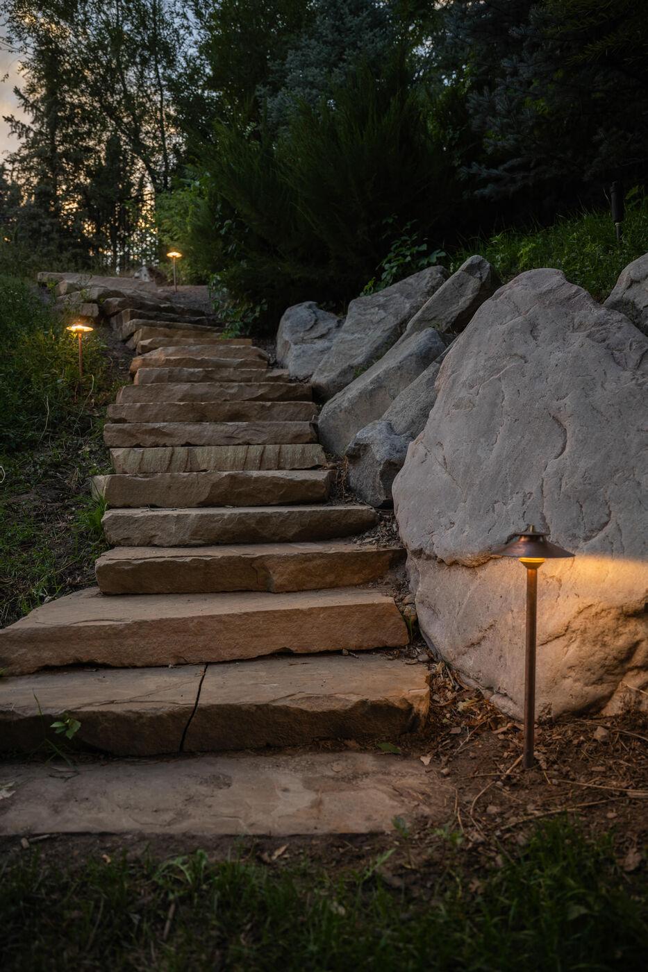 Lit stone steps climbing past a boulder outcrop at dusk