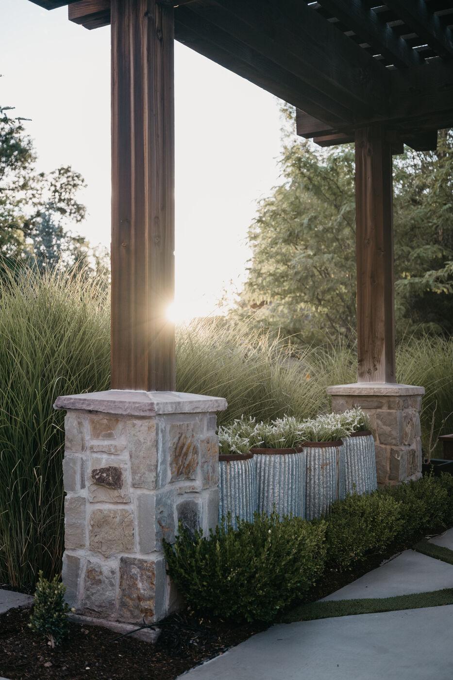 A stone pier carrying a pergola above ornamental grasses catching low sun