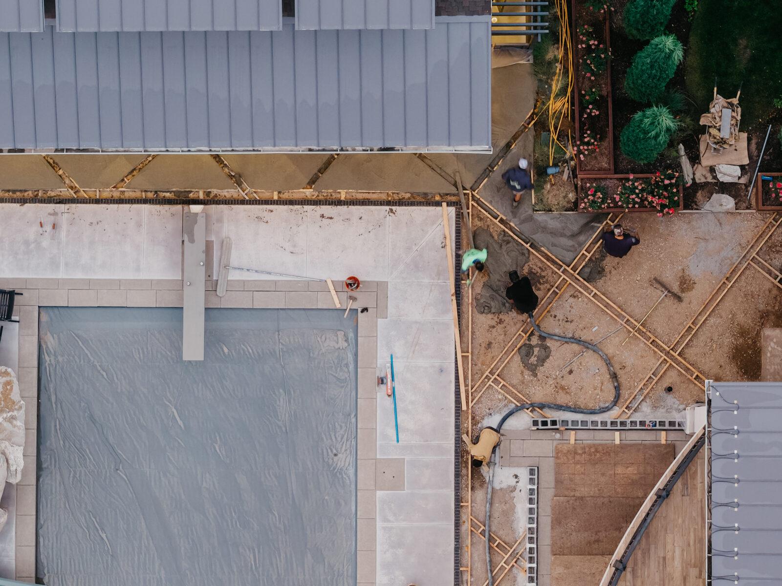 Overhead view of a back yard mid-build — compacted base poured and hardscape framed before surfacing