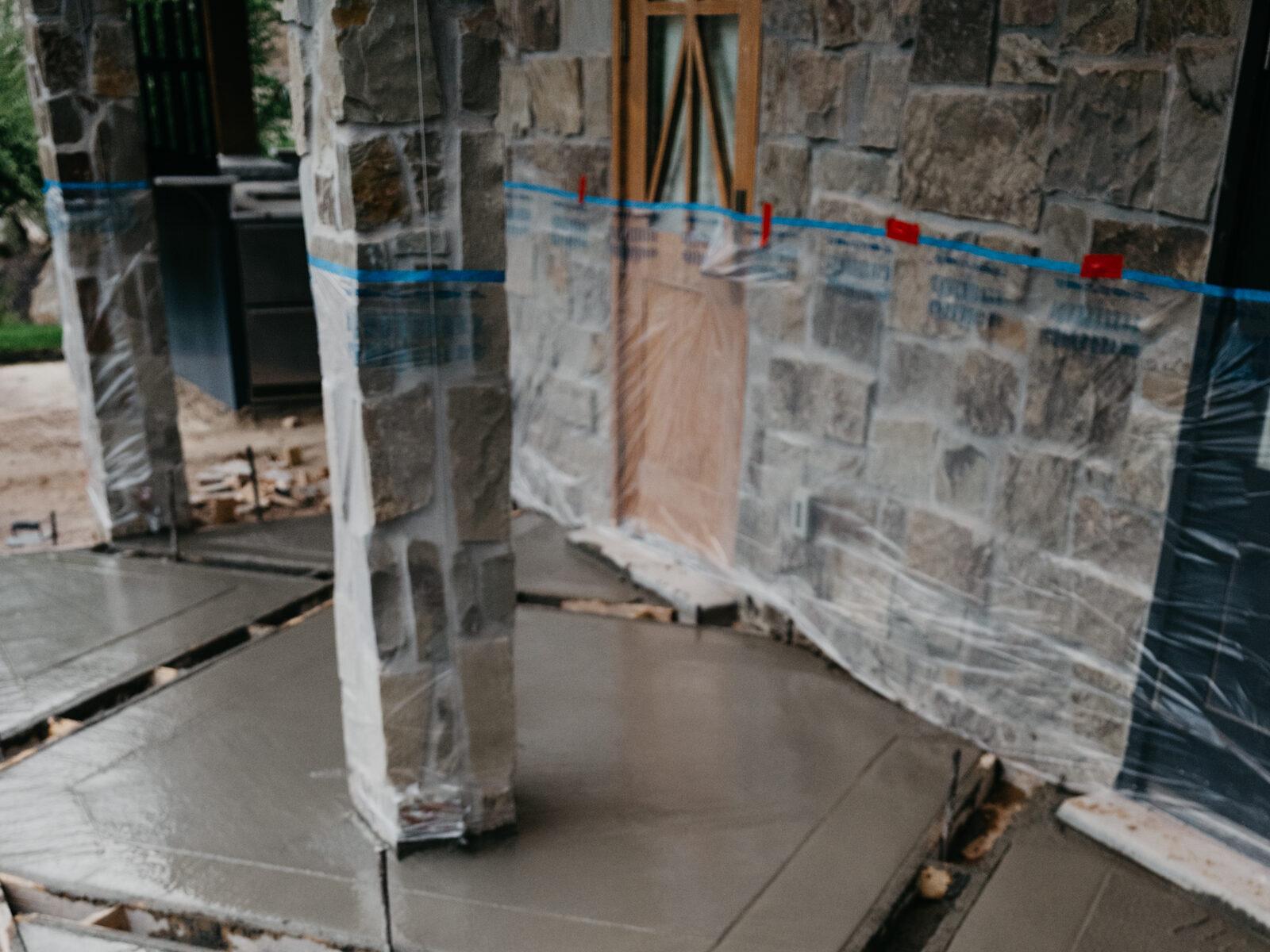 A channel drain set into fresh concrete along a stone-clad wall wrapped for protection