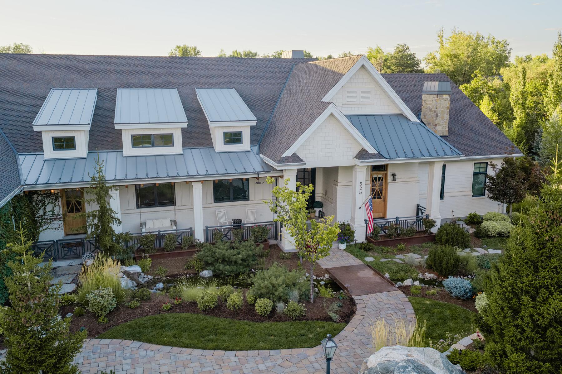 The front of a white house with layered planting and a paver walk to the door