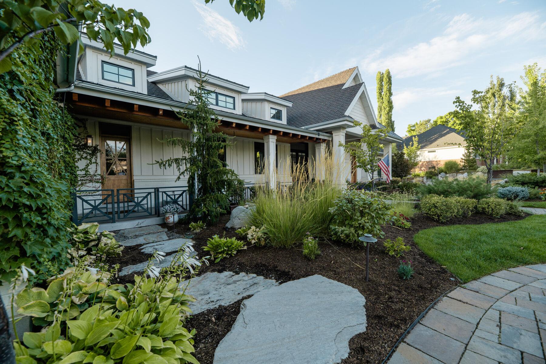 A covered porch behind massed planting and a broad stone path