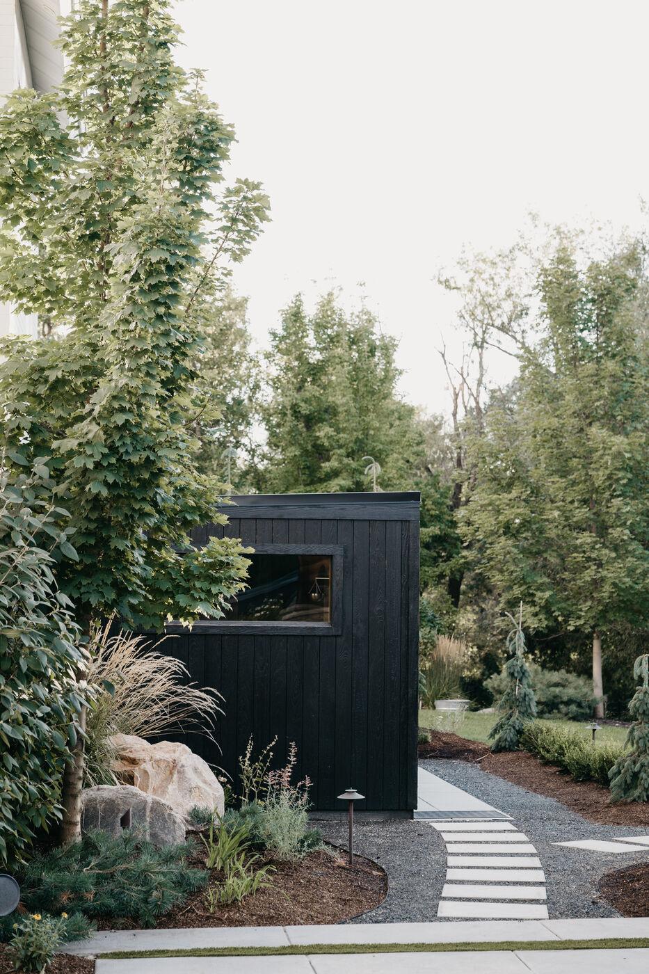 A blackened-timber structure at the end of a stone path among young trees