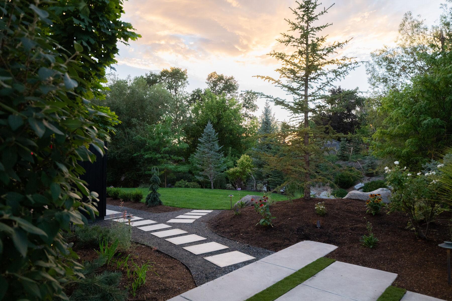 A stepping-stone path crossing lawn at sunset between deep planted borders