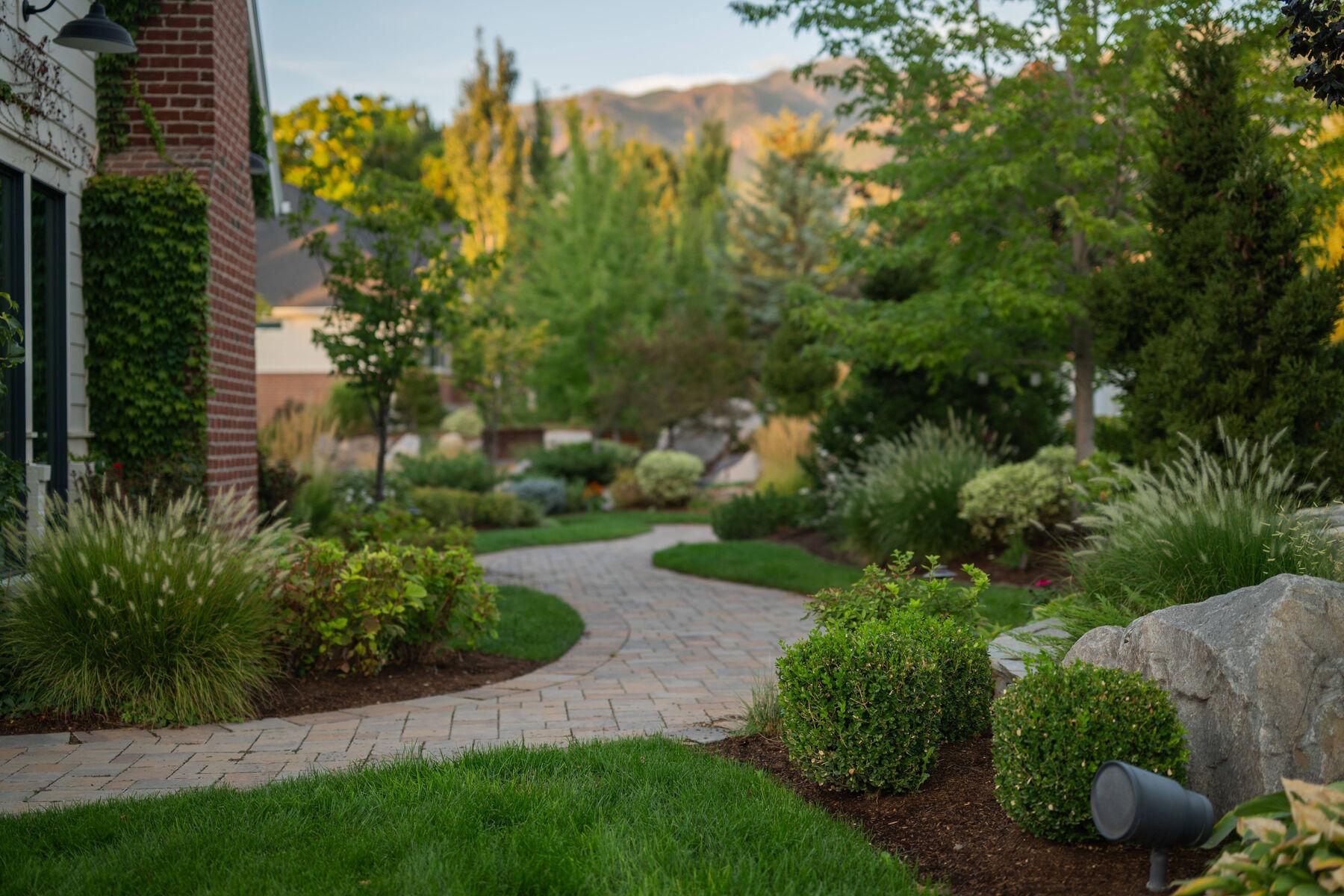 A curved paver path through grasses and clipped shrubs with mountains beyond