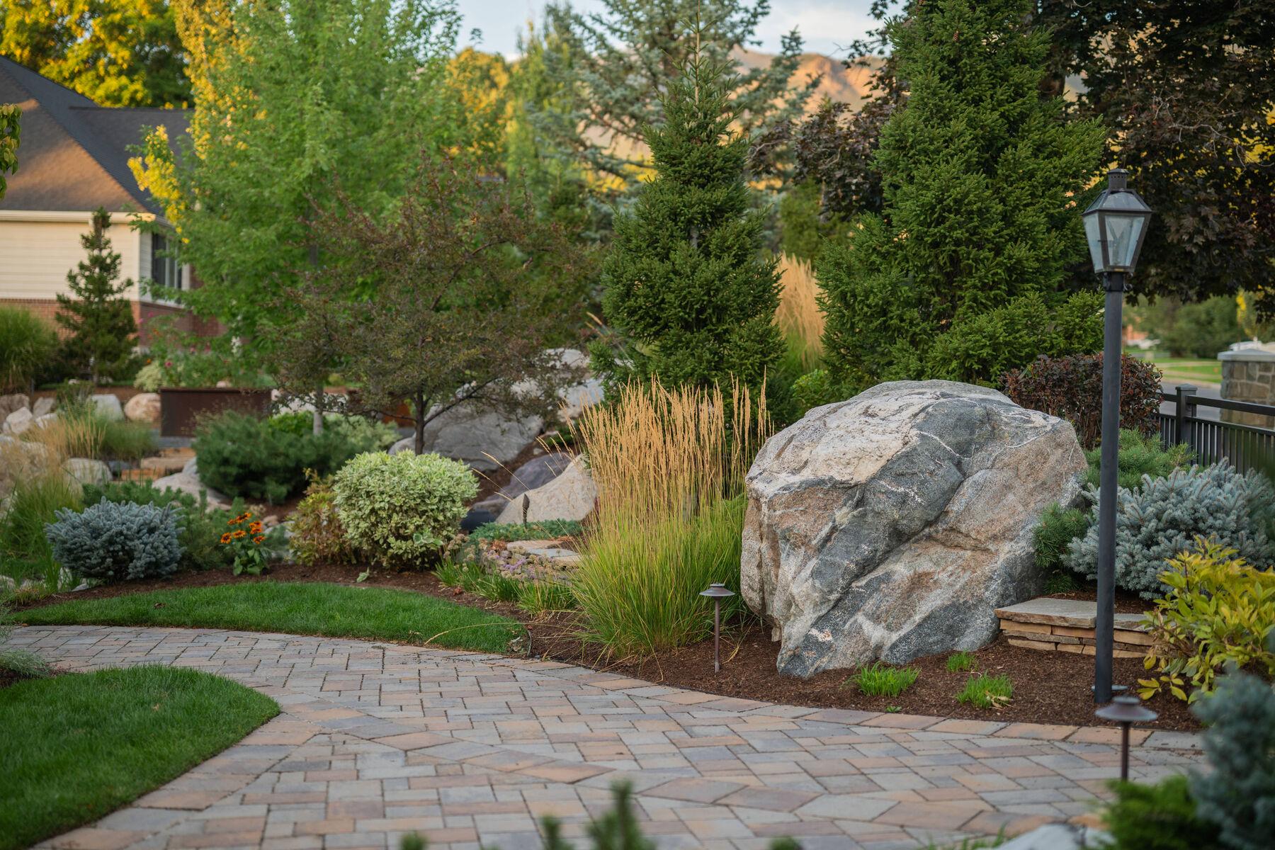 A set boulder anchoring the edge of a paver terrace and its mixed planting