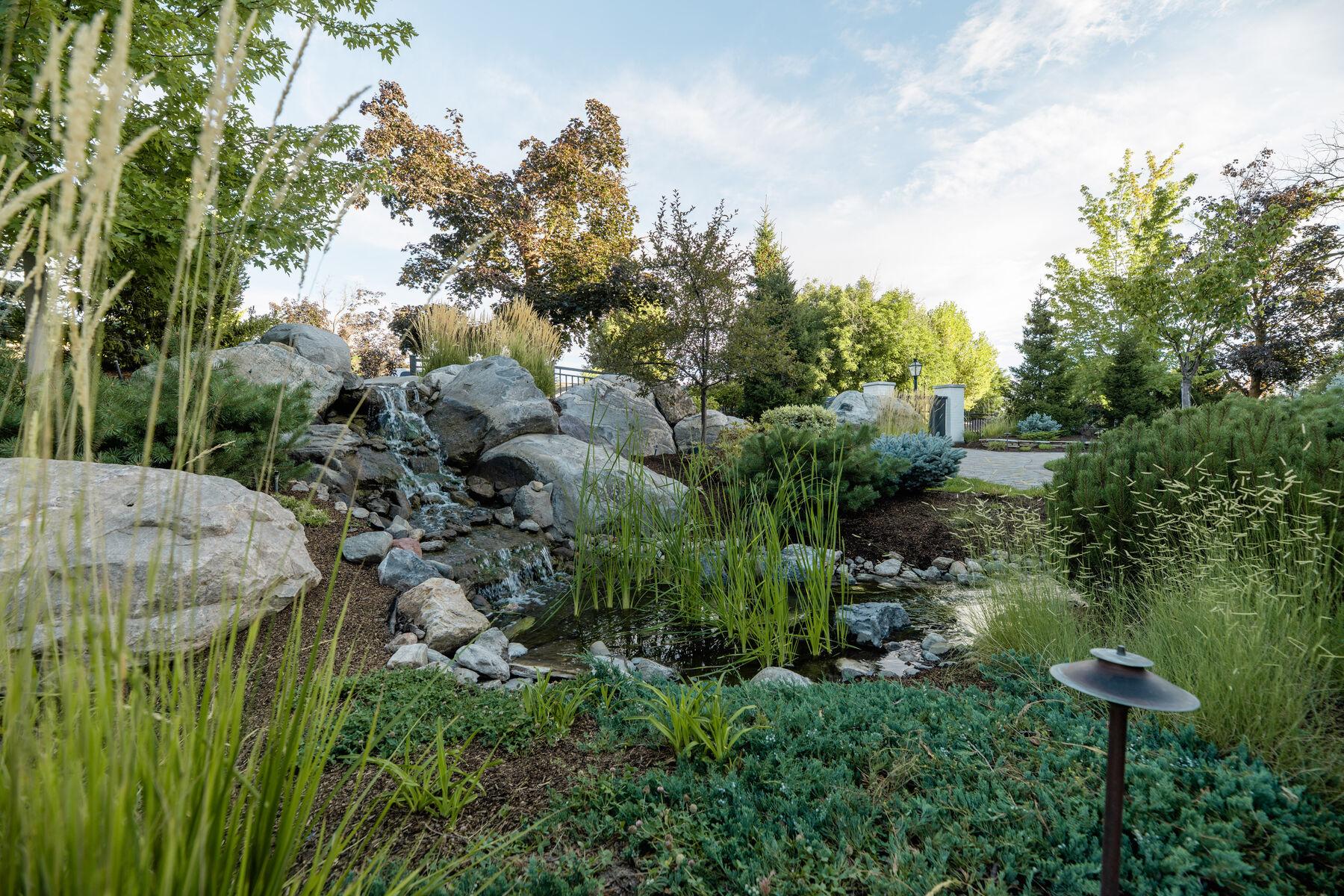 A boulder-edged pond with marginal grasses and a low path light at its rim